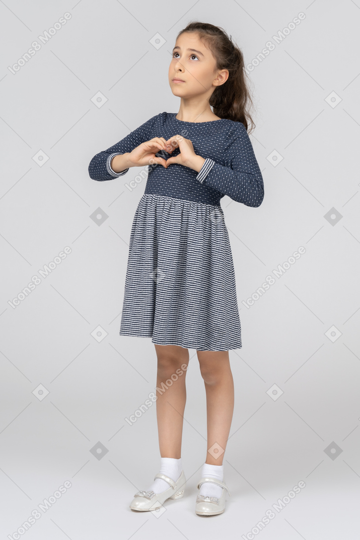 Little girl in blue dress and white shoes showing heart hands