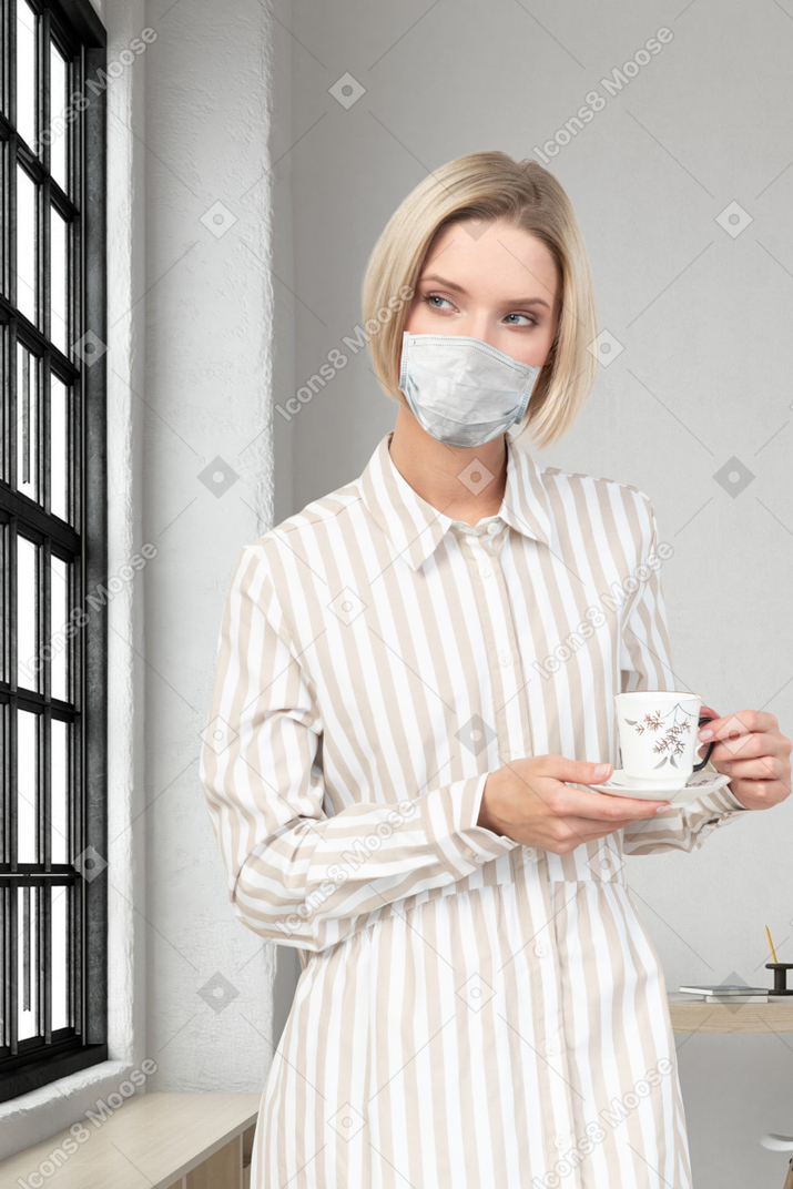 A woman wearing a mask holding a cup of coffee