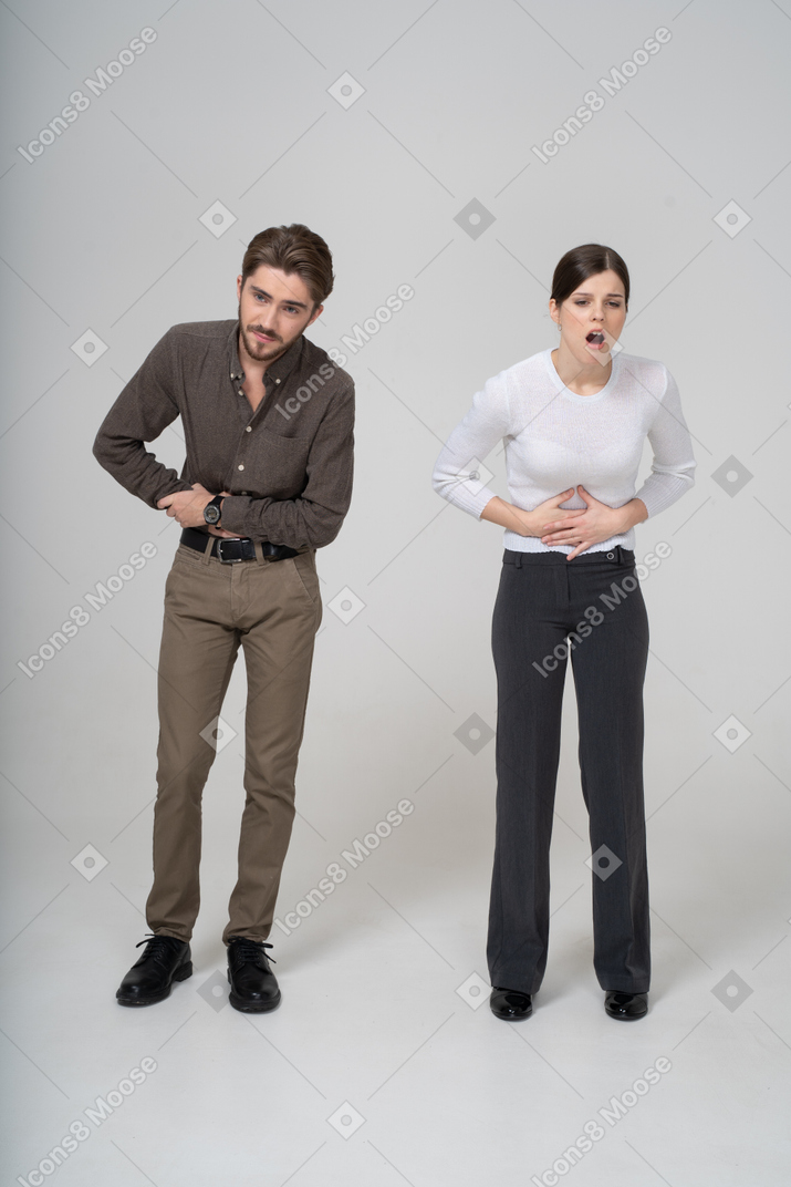 Vista frontale di una giovane coppia in abiti da ufficio che tocca lo stomaco