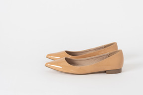 Una foto lateral de un par de zapatos de tacón bajo de laca beige