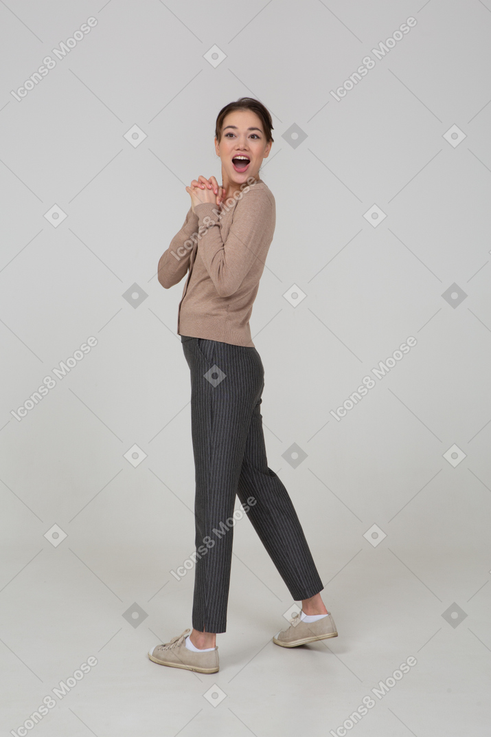 Three-quarter back view of a delighted young lady in beige pullover holding hands together while turning away