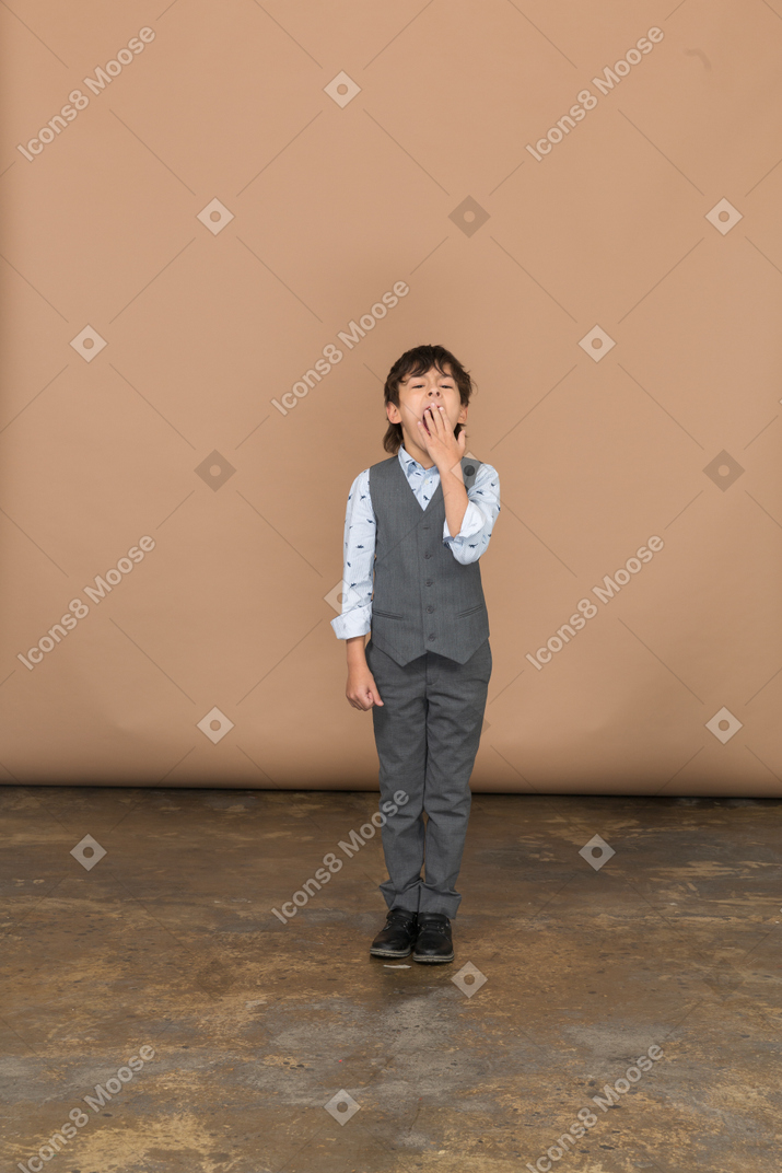 一个穿着西装的男孩打哈欠用手捂住嘴的前视图