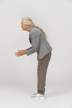 Вид сбоку на счастливую старушку в костюме, наклонившуюся и жестикулирующую