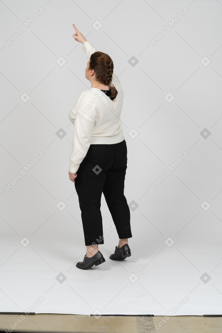 Rear view of a plump woman in casual clothes standing with raised arm