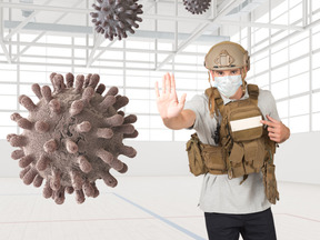 A man wearing a hard hat and a face mask showing stop hand gesture to a coronavirus floating in the air
