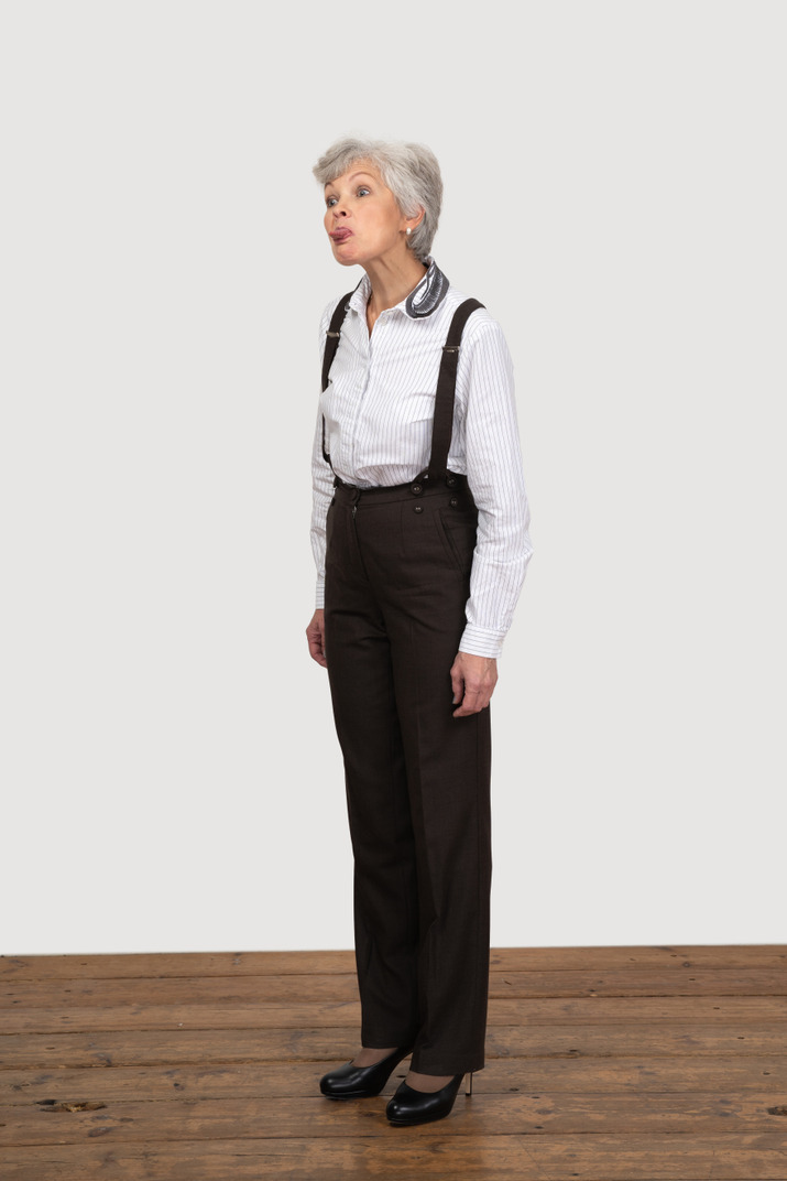 Three-quarter view of a teasing old woman in office clothing showing tongue