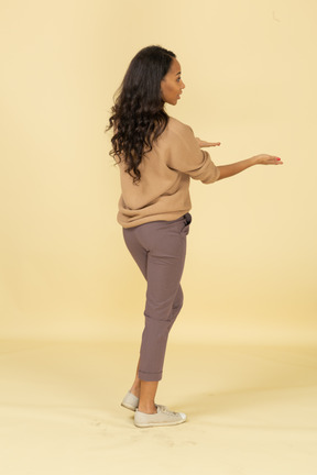 Three-quarter back view of a questioning dark-skinned young female outstretching hands