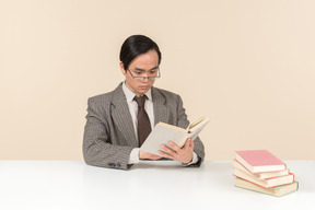 An asian teacher in a checkered suit, a tie and a book in his hand, working with the class