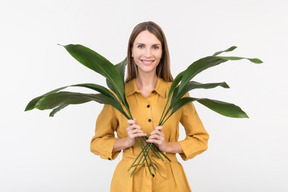 Souriante jeune femme tenant des feuilles vertes dans les deux mains