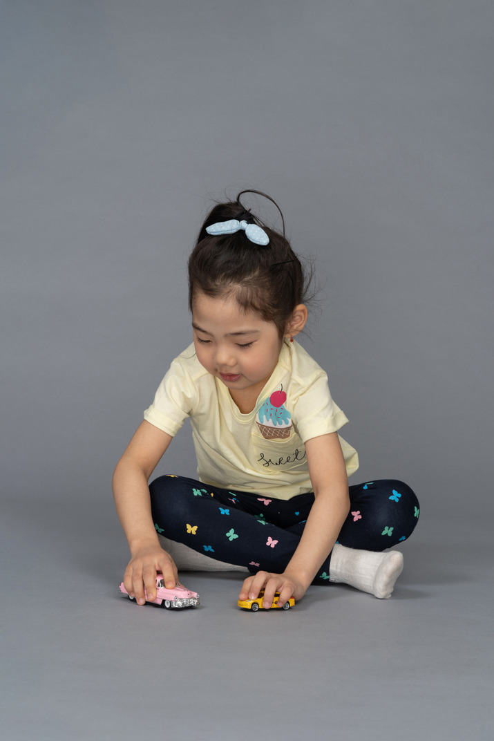 Little girl playing with toy cars while sitting on the floor
