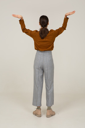 Vista posteriore di una giovane donna asiatica in calzoni e camicetta che alza le mani