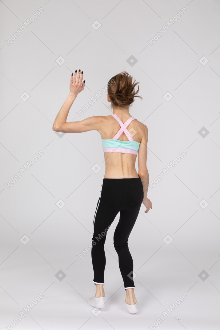 Back view of a teen girl in sportswear jumping and waving hand