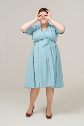Front view of a woman in blue dress looking through imaginary binoculars
