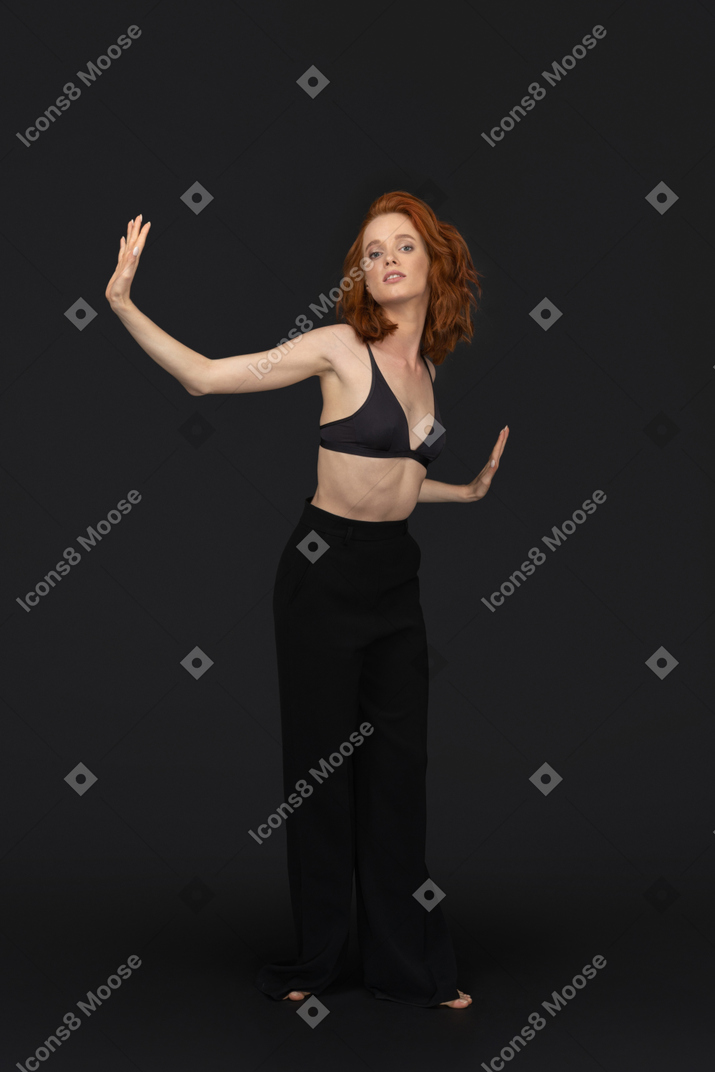 A frontal view of the cute young woman dancing on the black background and posing