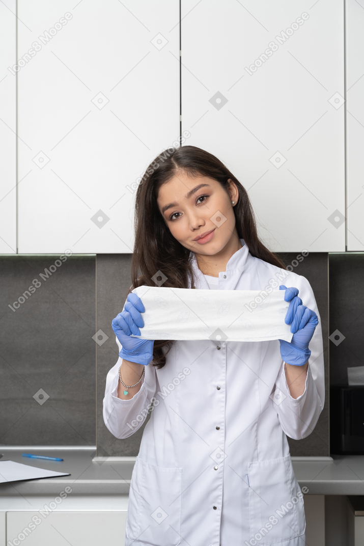 Vista frontal de una doctora complacida mirando a la cámara y sosteniendo un paño blanco en guantes protectores