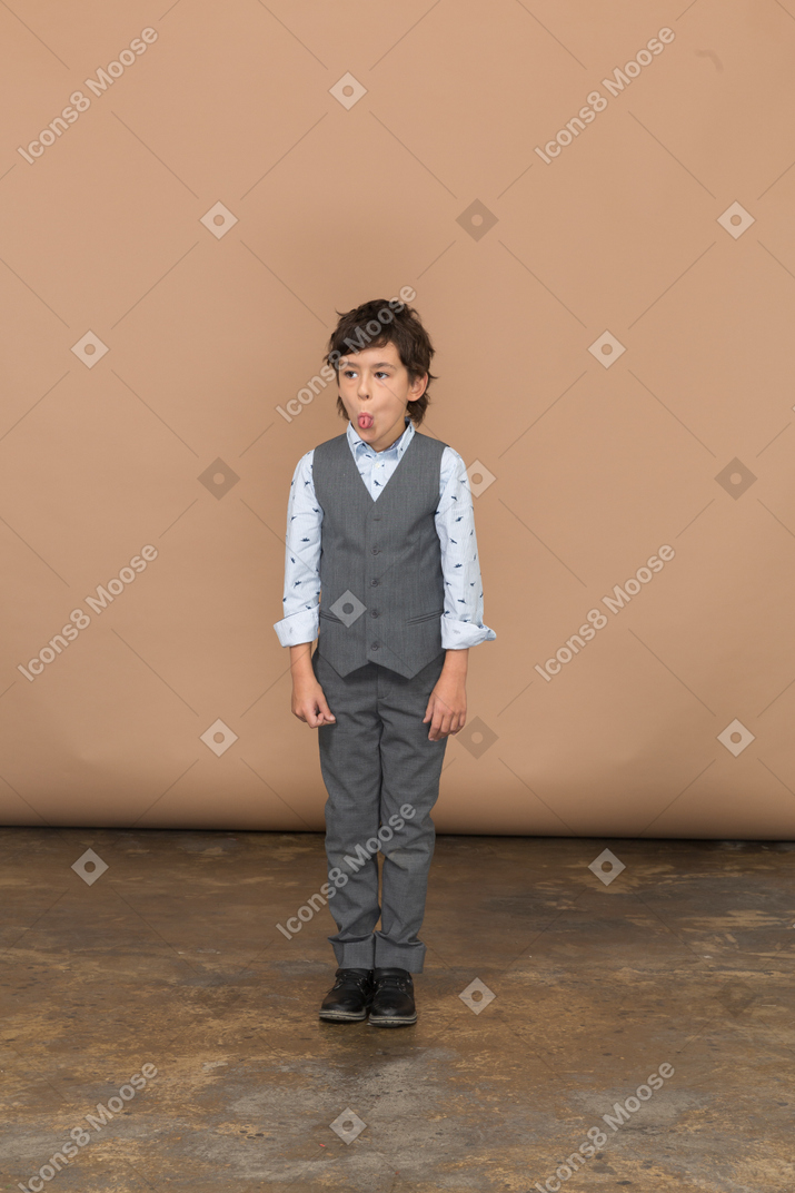 Vista frontale di un ragazzo carino in abito grigio che sta fermo e fa delle smorfie