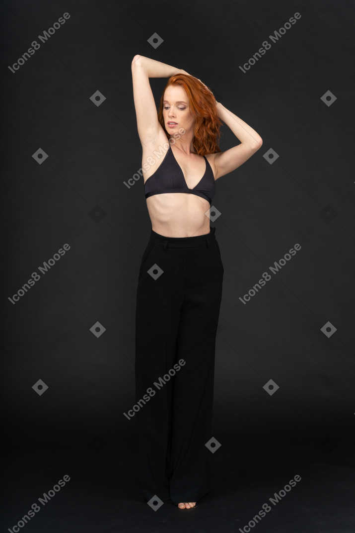 A frontal view of the young sexy woman on the black background holding her hands behind the head