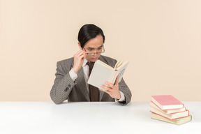 An asian teacher in a checkered suit, a tie and a book in his hand, working with the class