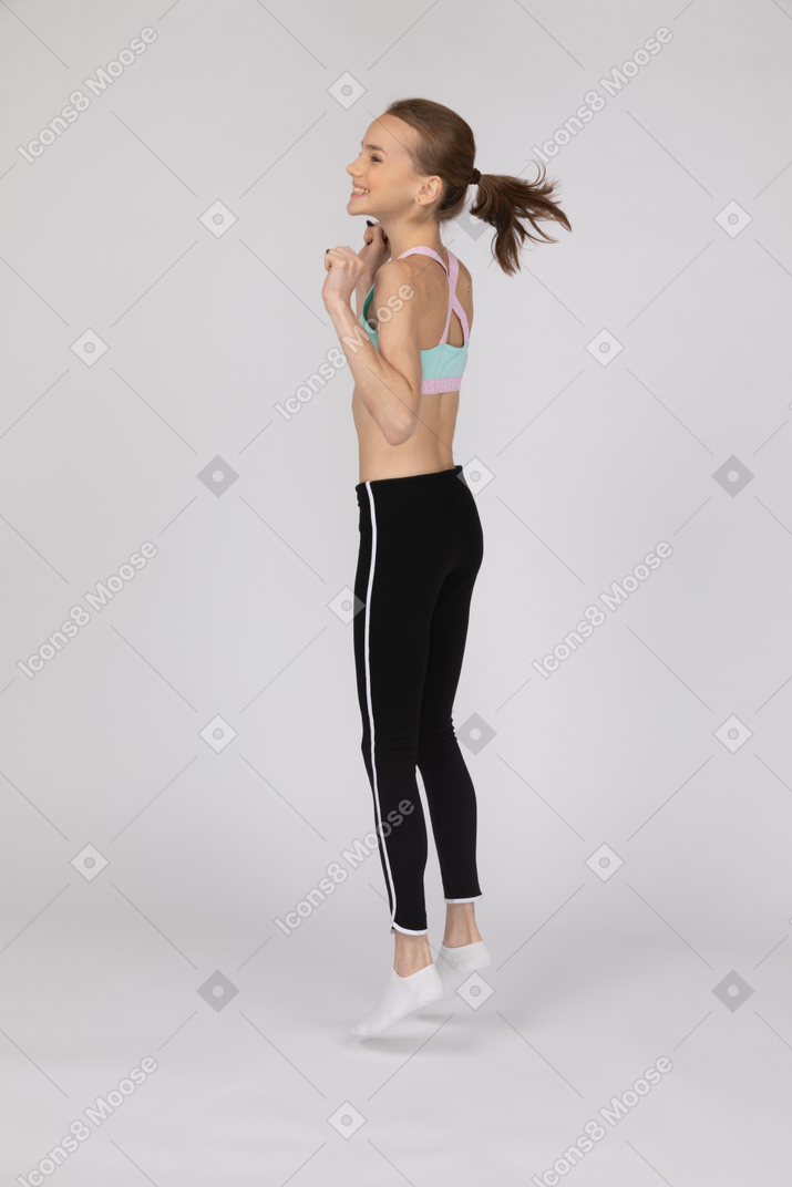 Вид сбоку на взволнованную девушку-подростка в спортивной одежде, прыгающую