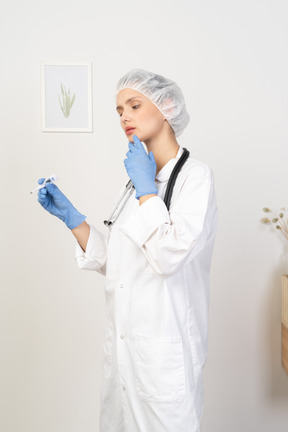 Three-quarter view of a perplexed young female doctor with stethoscope holding thermometer