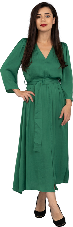 Vista frontal de uma jovem de vestido verde colocando a mão no quadril