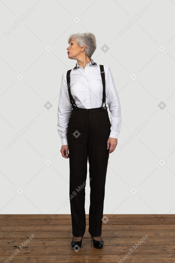 脇を見ながら屋内でじっと立っている事務服を着た老婆の正面図