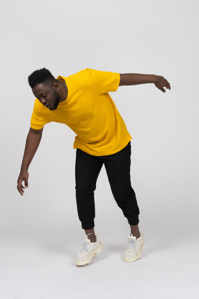 Three-quarter view of a young dark-skinned man in yellow t-shirt leaning forward & outstretching arm