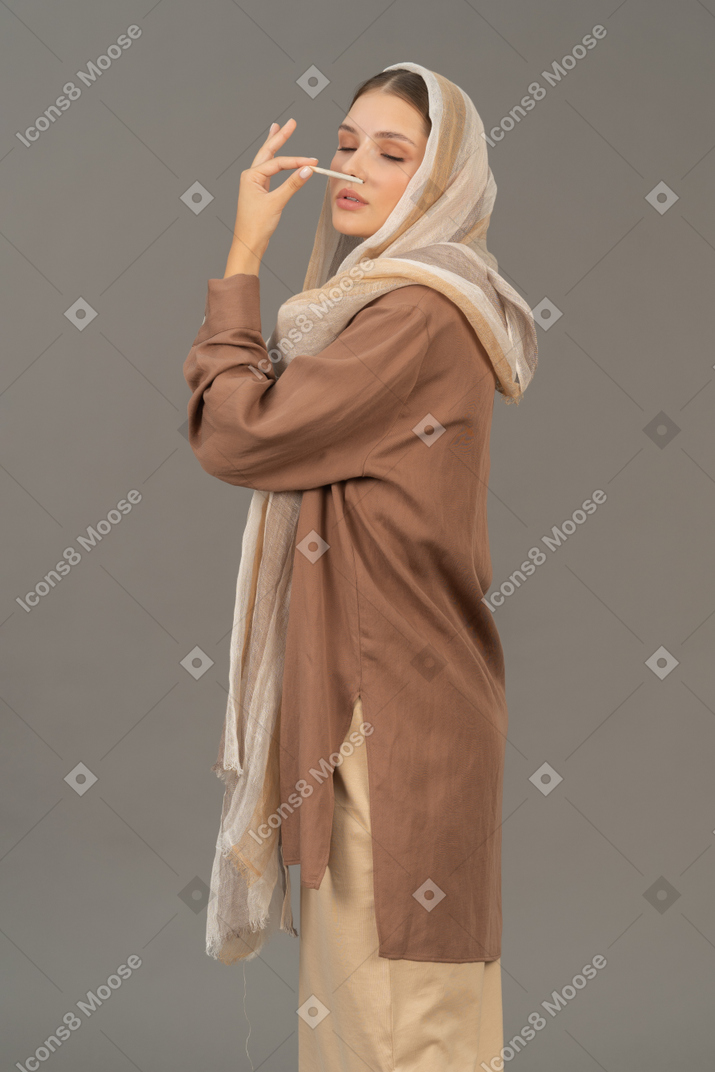 Young woman in beige clothes smelling a cigarette