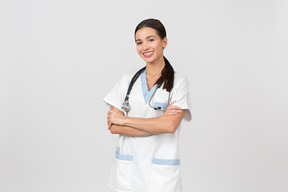 Sorrindo jovem médico feminino em pé com as mãos cruzadas