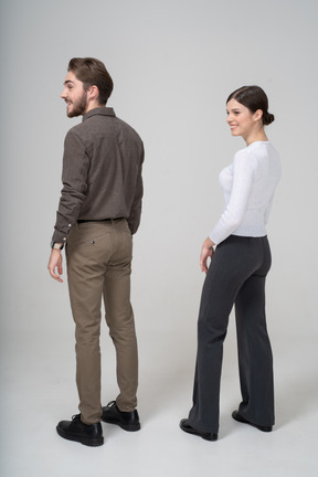 Vista posterior de tres cuartos de una joven pareja encantada en ropa de oficina