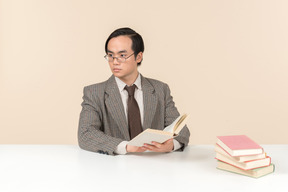 An asian teacher in a checkered suit, a tie and a book in his hand, working with the class