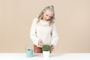 Улыбающаяся пожилая женщина ухаживает за растением