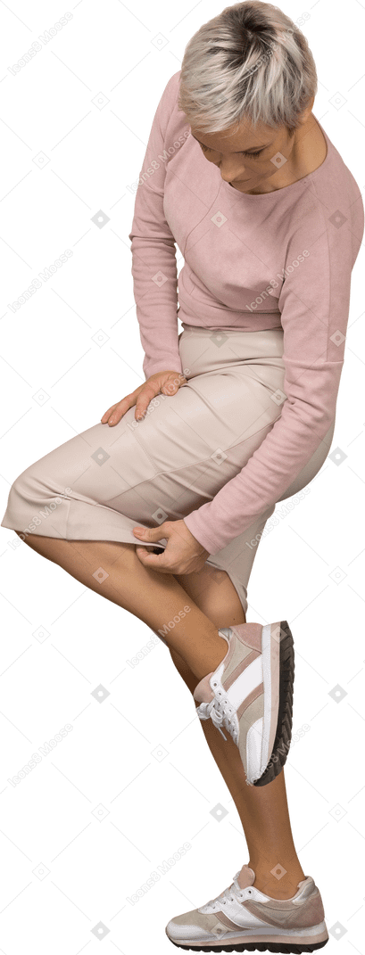 Vista lateral de una mujer en ropa casual de pie con la pierna levantada y mirando su falda