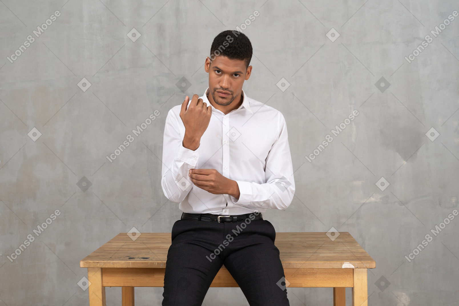 Mann in formeller kleidung sitzt auf einem tisch und fixiert seine manschette