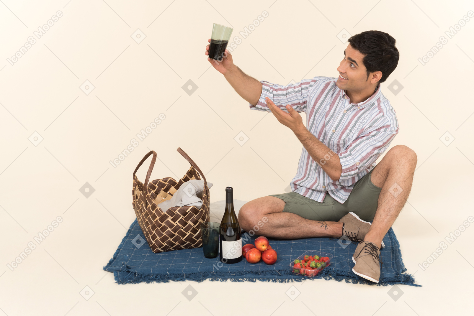 Joven caucásico sentado en una manta y bebiendo vino