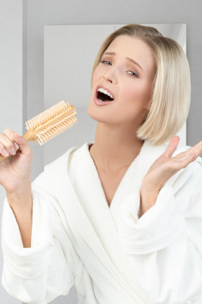 A woman in a bathrobe singing into a hairbrush