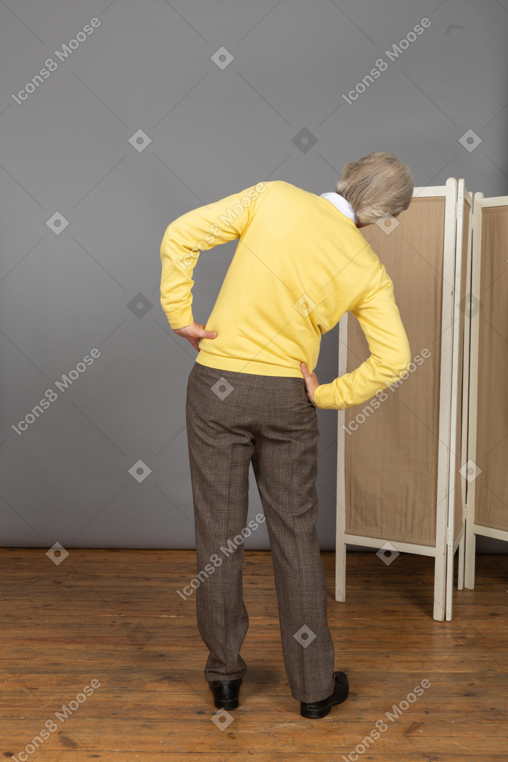 Vista posteriore di un uomo anziano che mette le mani sui fianchi mentre si inclina da parte