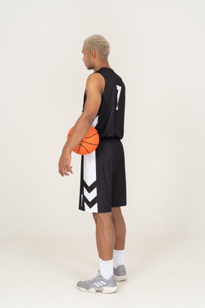 ボールを持っている若い男性のバスケットボール選手の4分の3の背面図