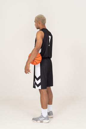 Three-quarter back view of a young male basketball player holding a ball