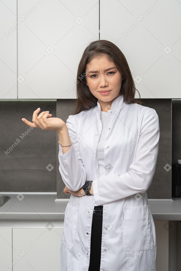 Front view of a questioning female doctor narrowing brows and raising hand