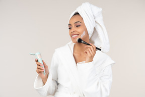 Black woman in white bathrobe and head towel enjoying her skin care routine