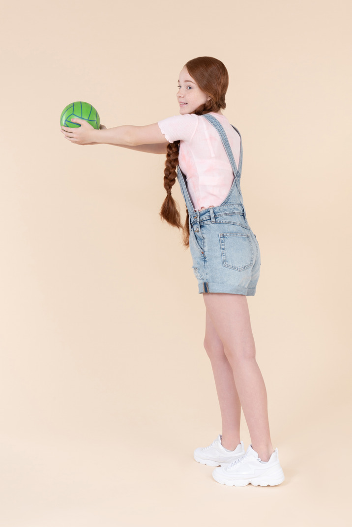Teenage girl standing half sideways and passing green ball she's holding