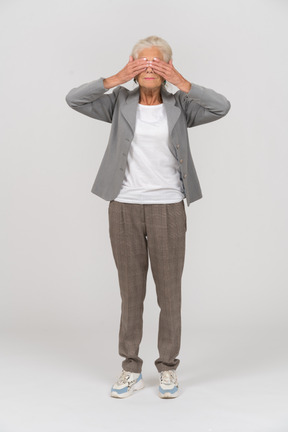 Vista frontal de una anciana en traje que cubre los ojos con las manos