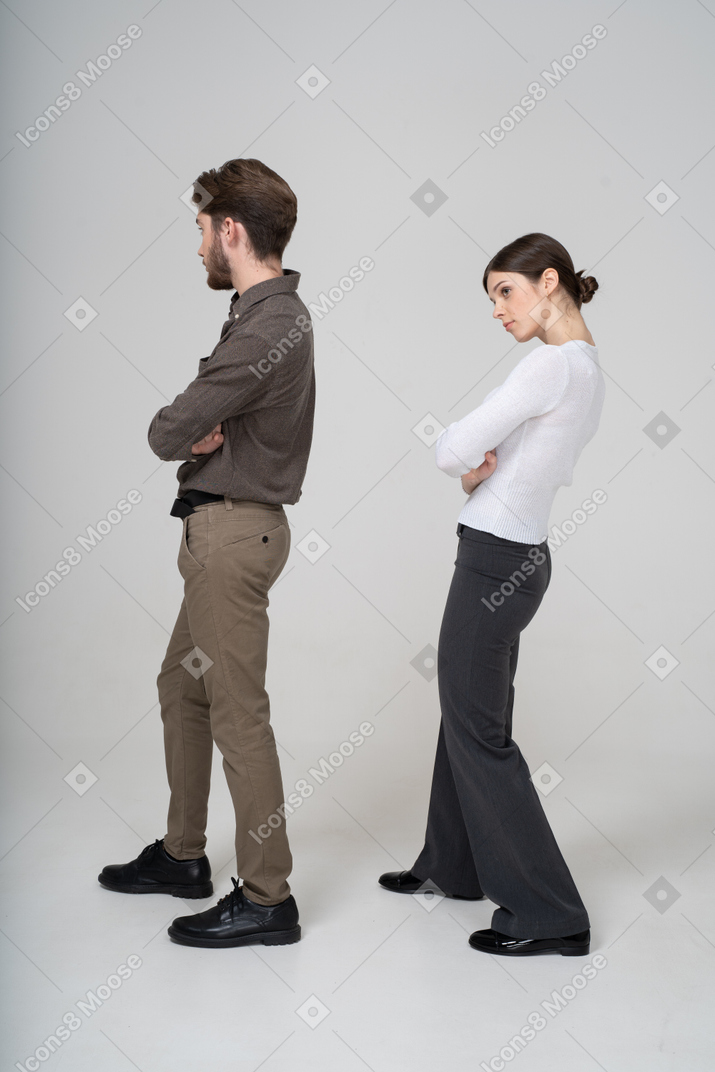 Vista traseira de três quartos de um jovem casal com roupas de escritório, cruzando os braços