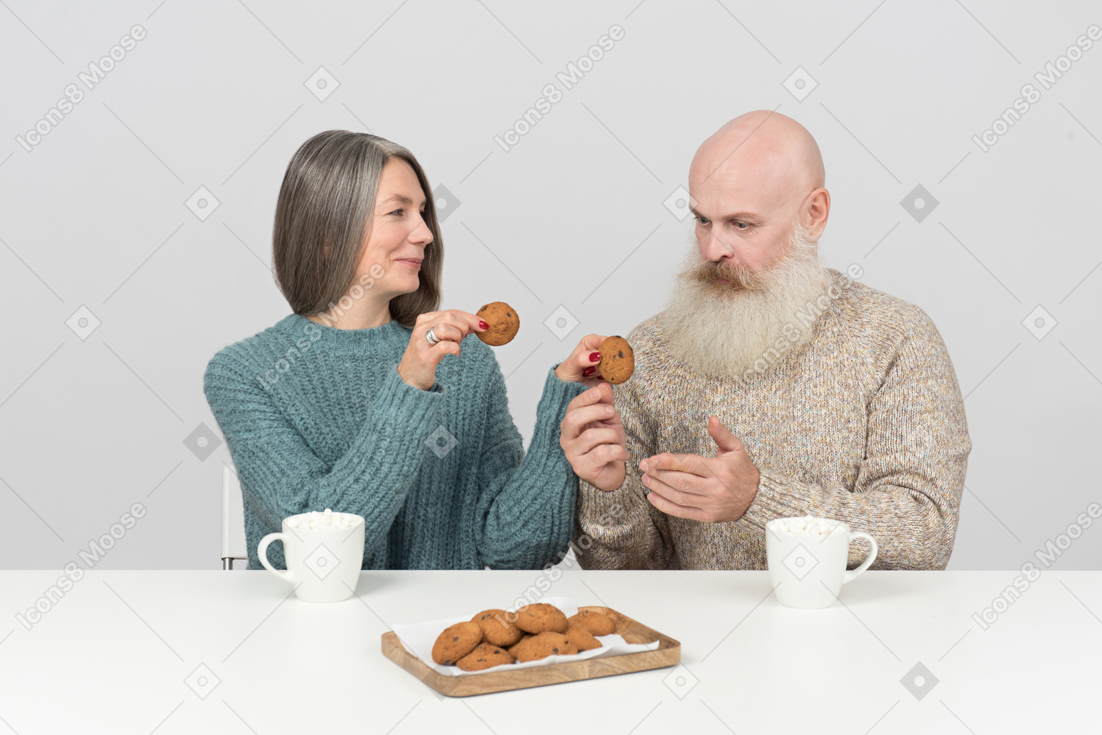 Elder woman giving one of two cookies she's holding to elder man