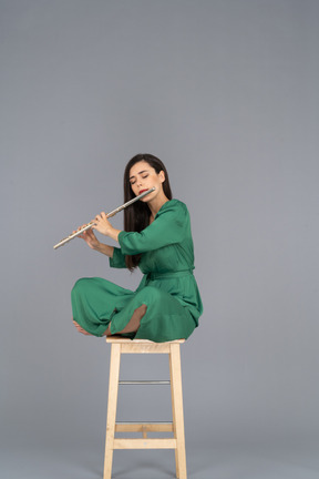 De cuerpo entero de una señorita tocando el clarinete sentada con las piernas cruzadas en una silla de madera