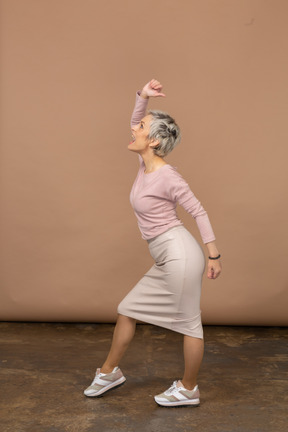 Side view of an emotional woman in casual clothes posing with raised arm