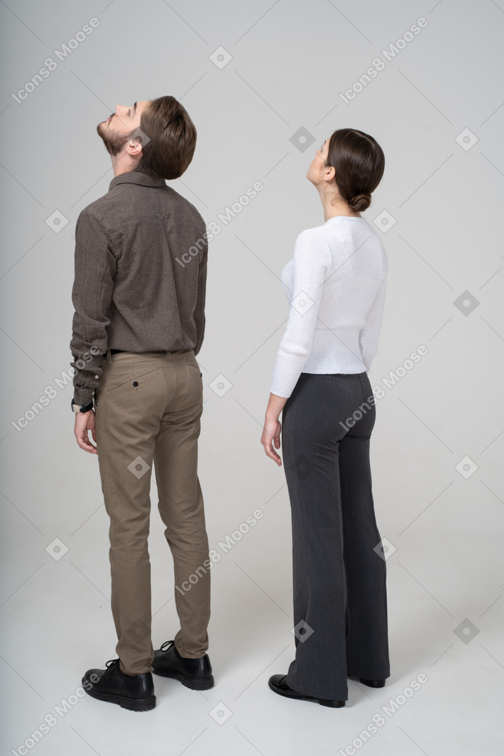 見上げるオフィス服の若いカップルの4分の3の背面図
