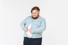 Joven con sobrepeso tratando de cerrar la camisa sobre él