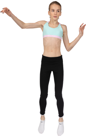 Vista frontal de uma adolescente em roupas esportivas levantando a mão e olhando para o lado enquanto pula